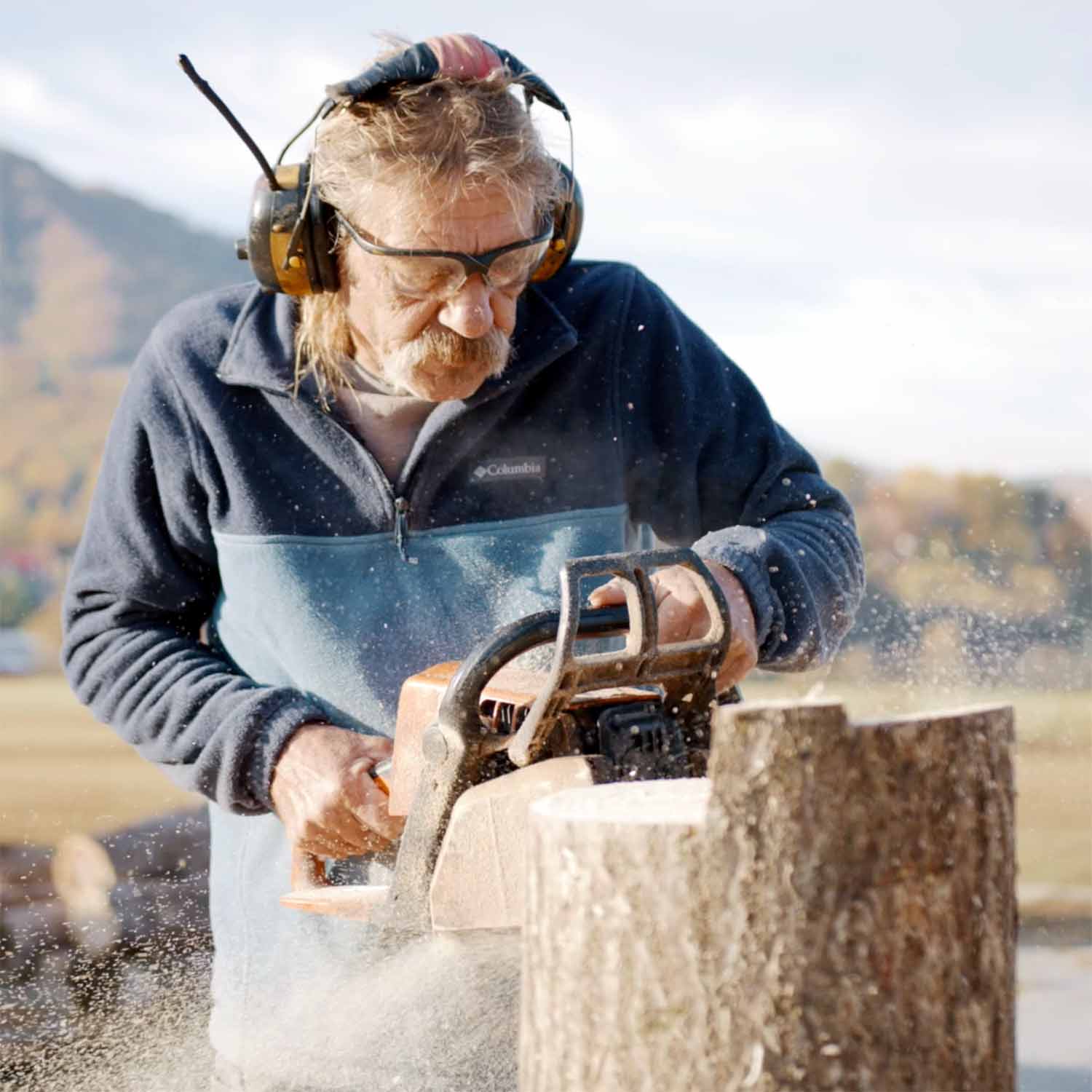 Tony carving sculptures from large blocks of wood with a chainsaw.
