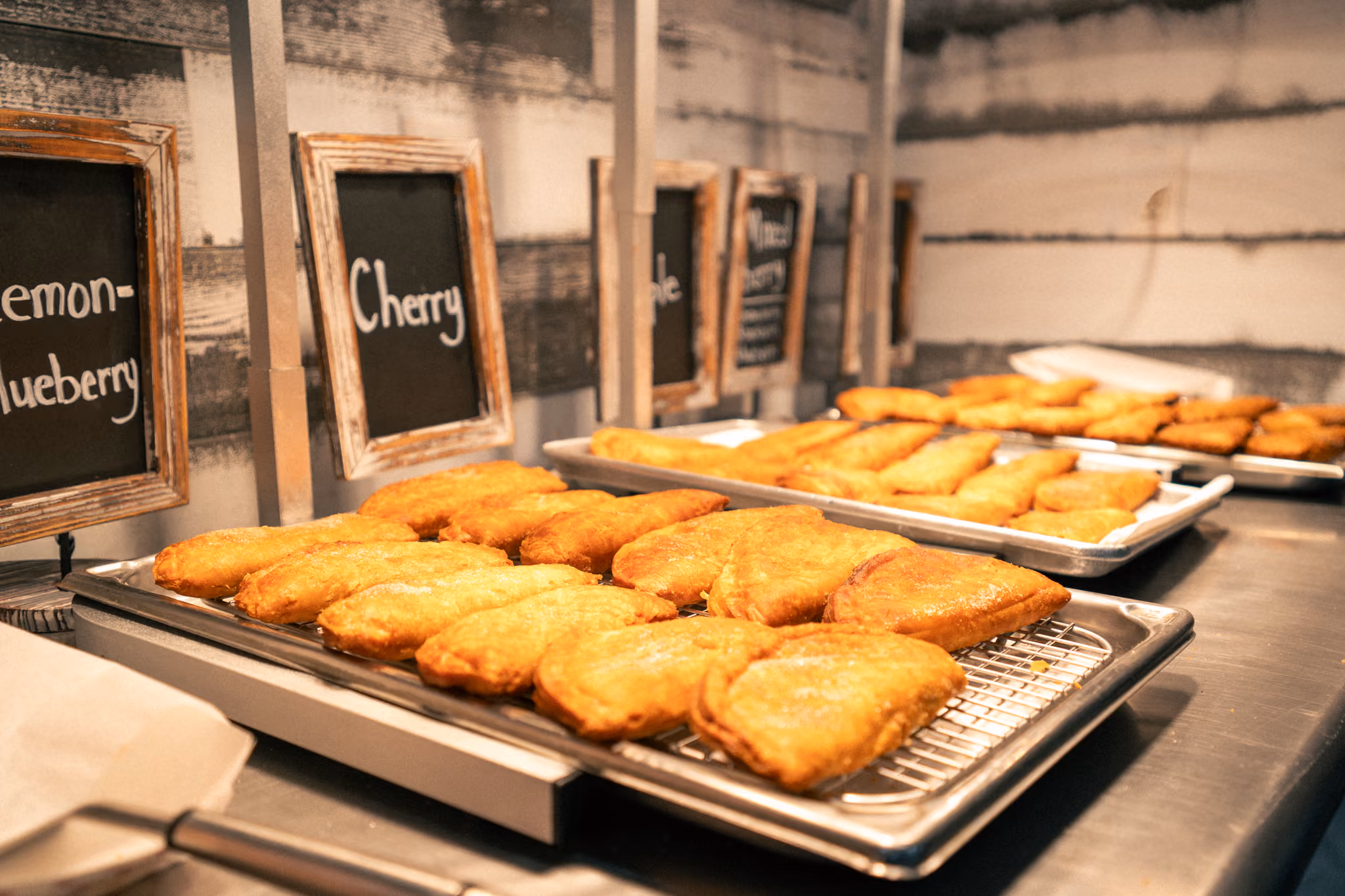 Close-up of powdered sugar being sprinkled over golden fried pies on a baking tray.