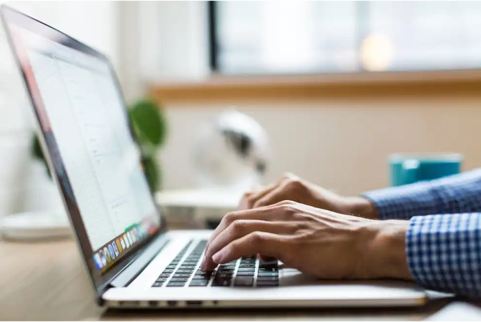 Person typing on a laptop keyboard at a desk with a blurred background.
