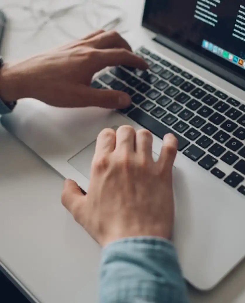 Hands of a person typing on a laptop keyboard with code displayed on the screen.