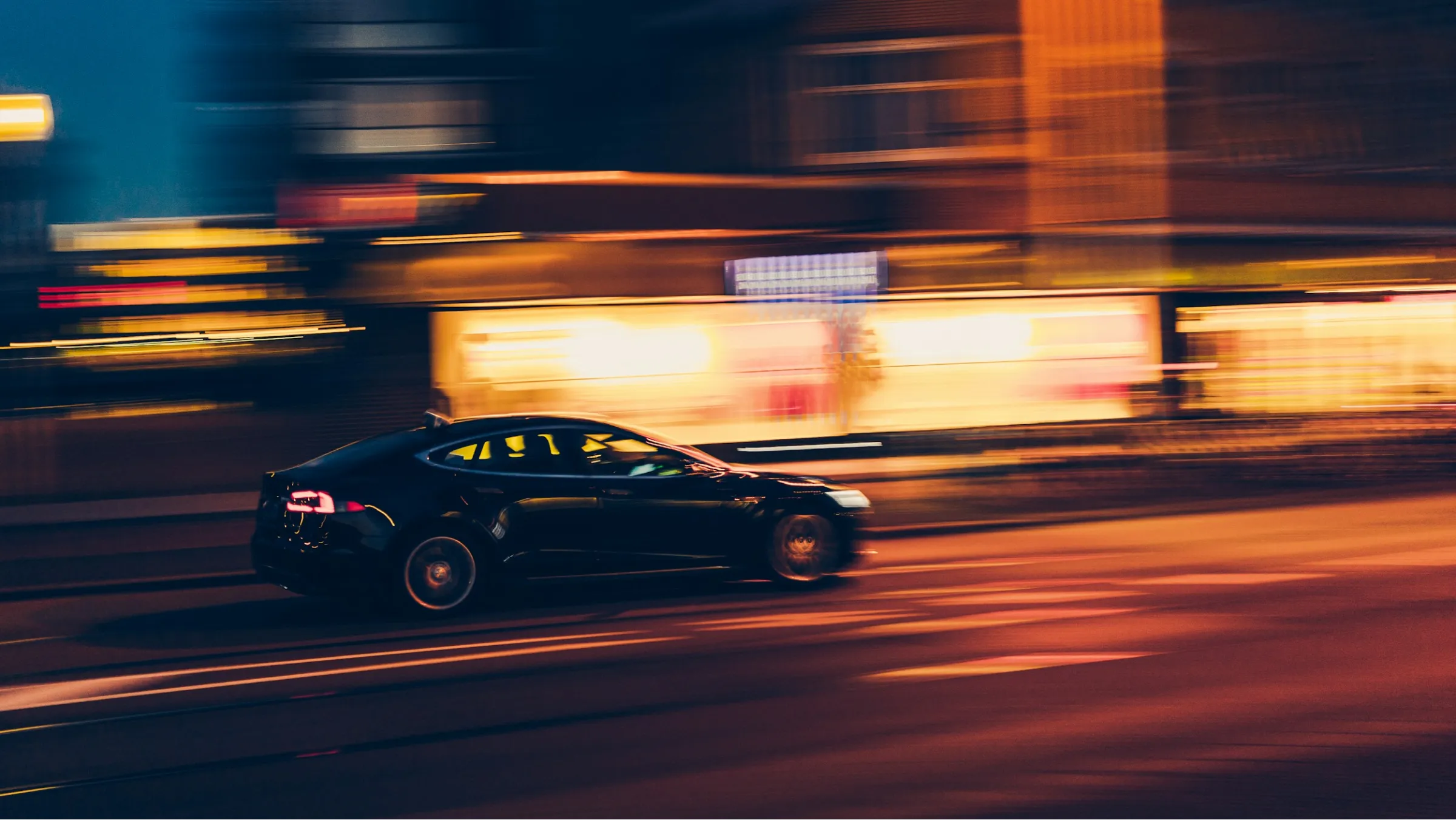 Black car speeding on a city street at night with blurred lights in the background.