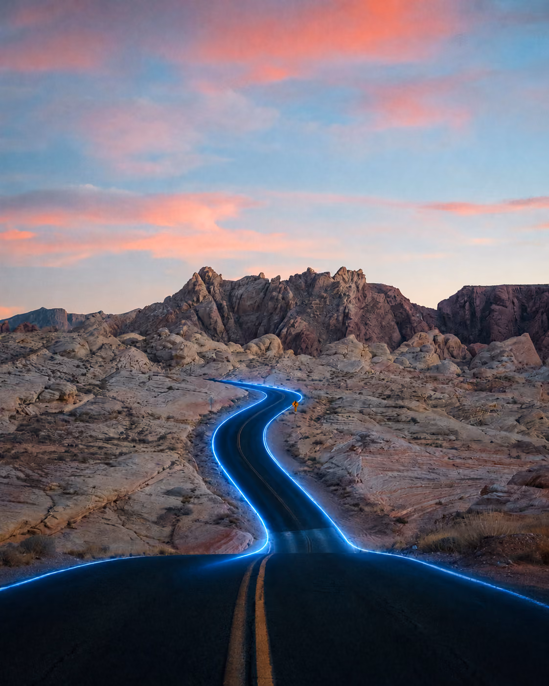 Winding desert road highlighted by a glowing blue light under a sunset sky with pink clouds.