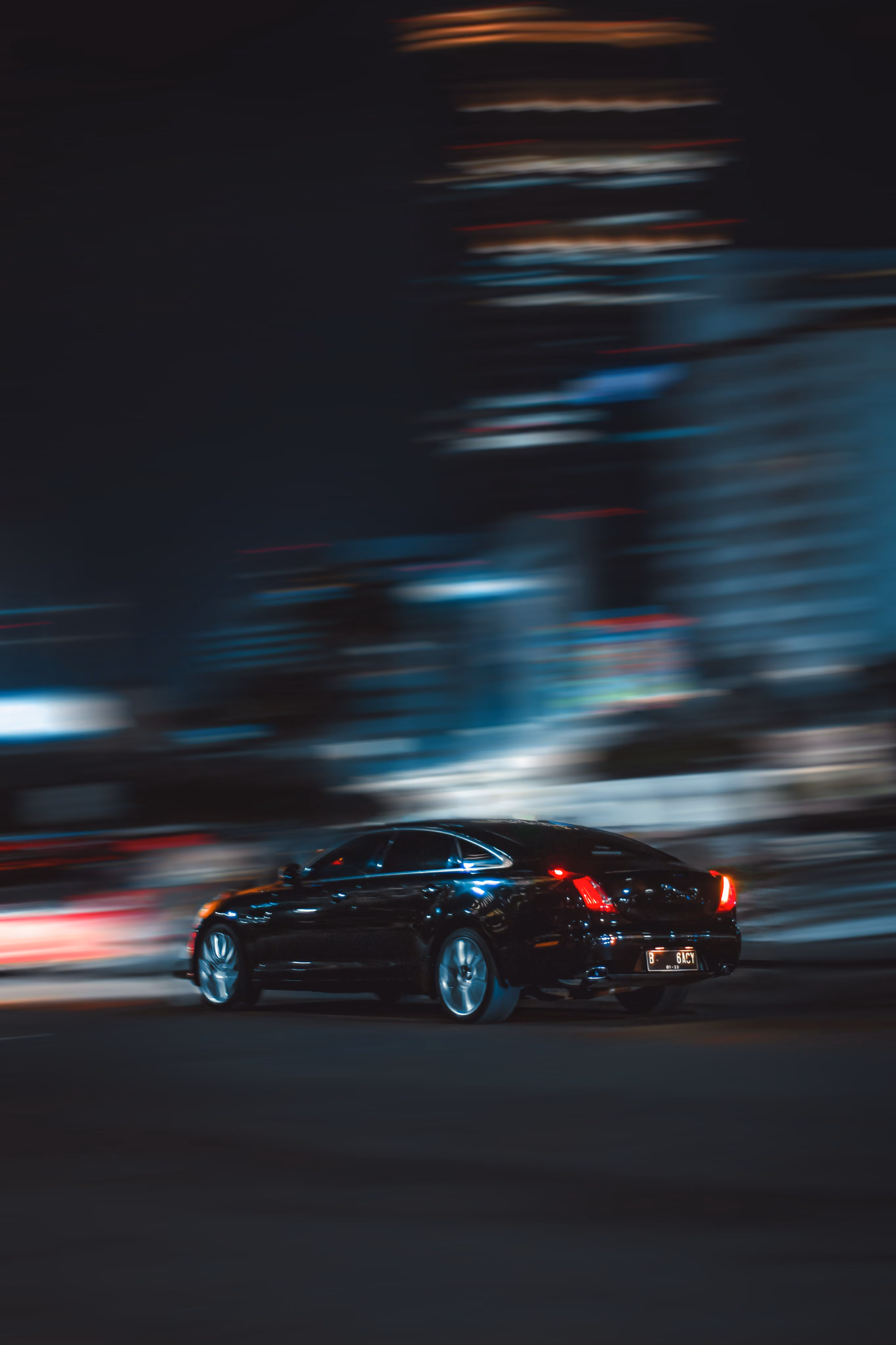 Black car driving fast at night with city lights blurred in the background.
