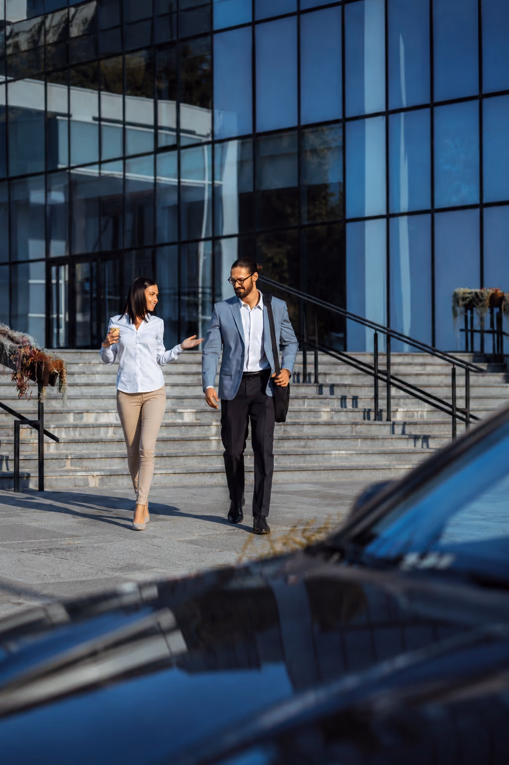 Two businesspeople walking and talking outside a modern glass building with stairs behind them.