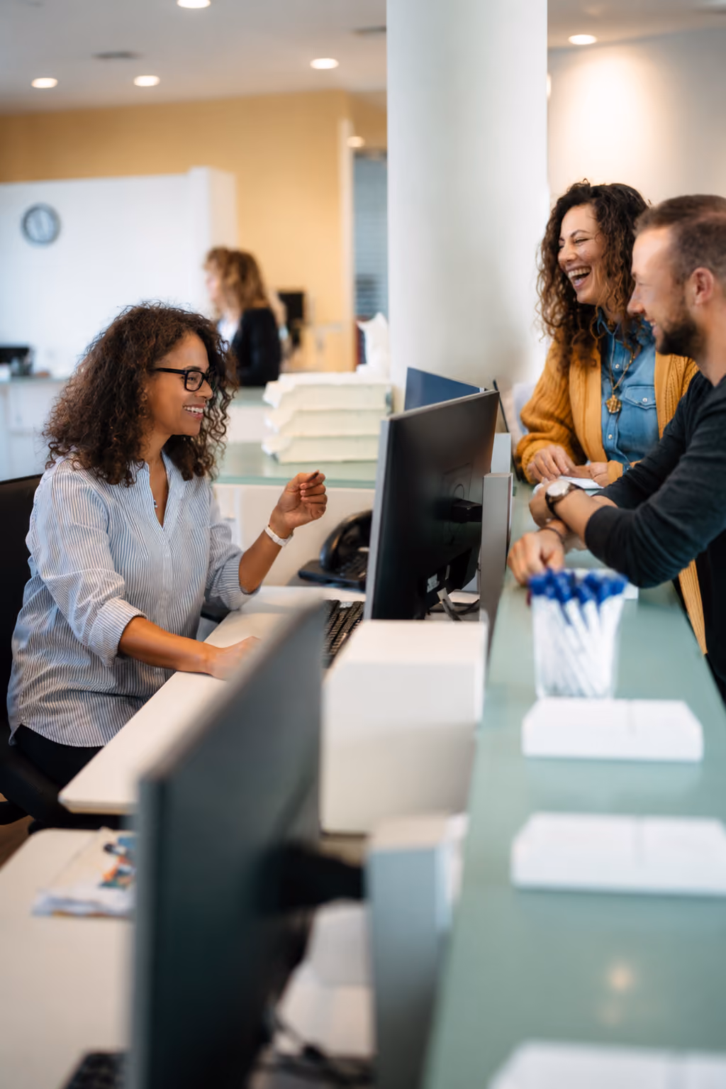 Smiling receptionist assisting a man and woman at a modern office front desk.