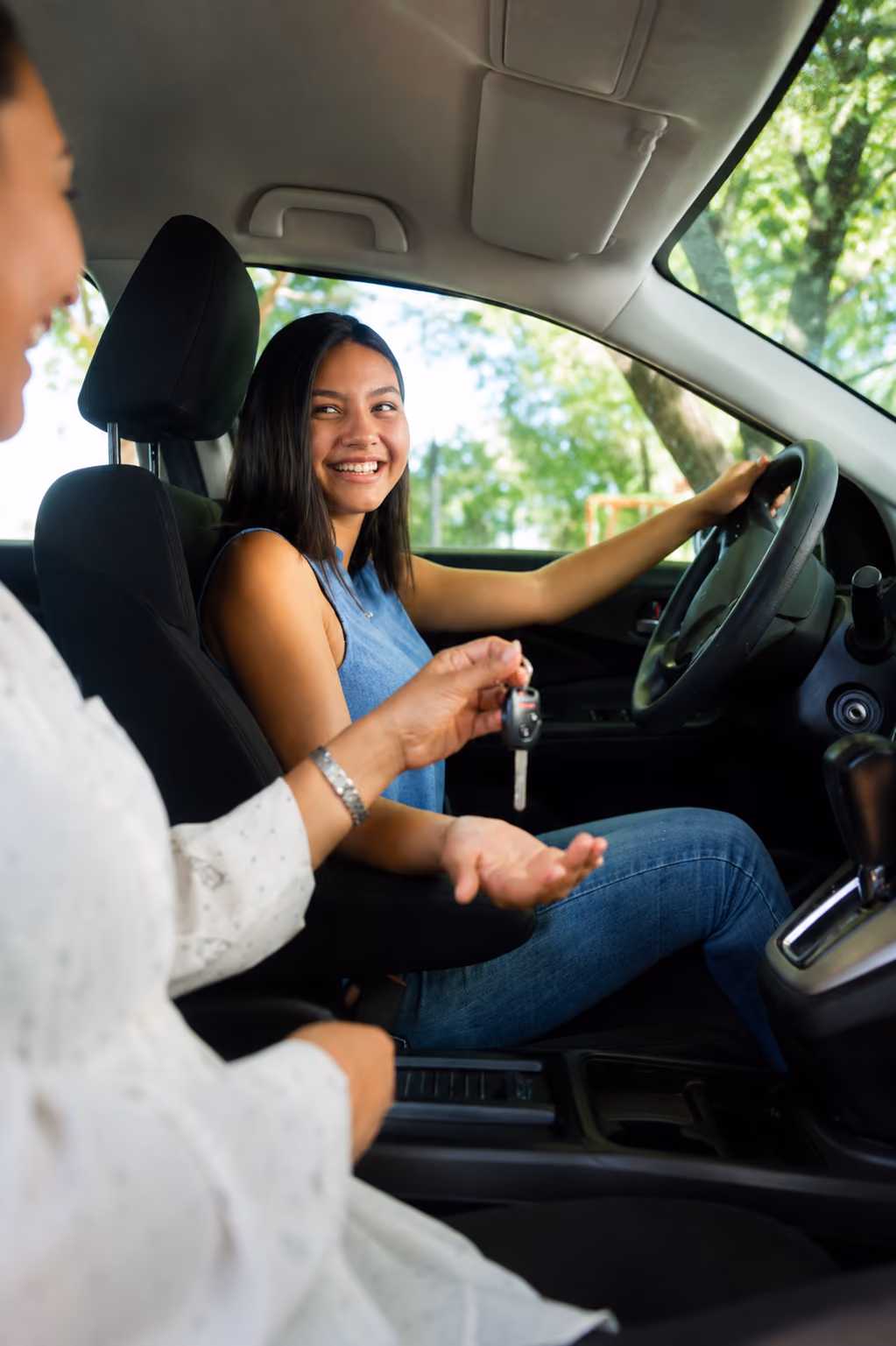 Woman in driver's seat smiling and receiving car keys from another person inside the car.