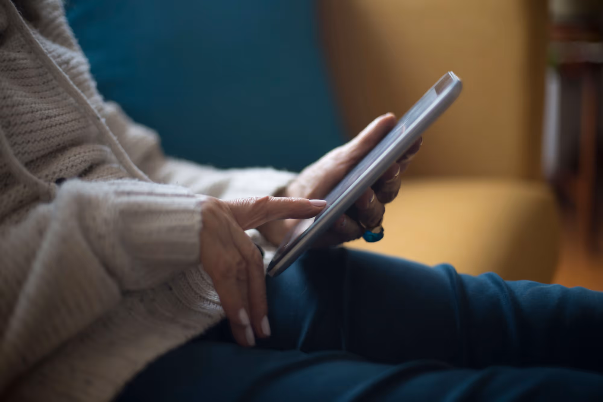 Person wearing a beige sweater using a tablet while sitting on a couch.
