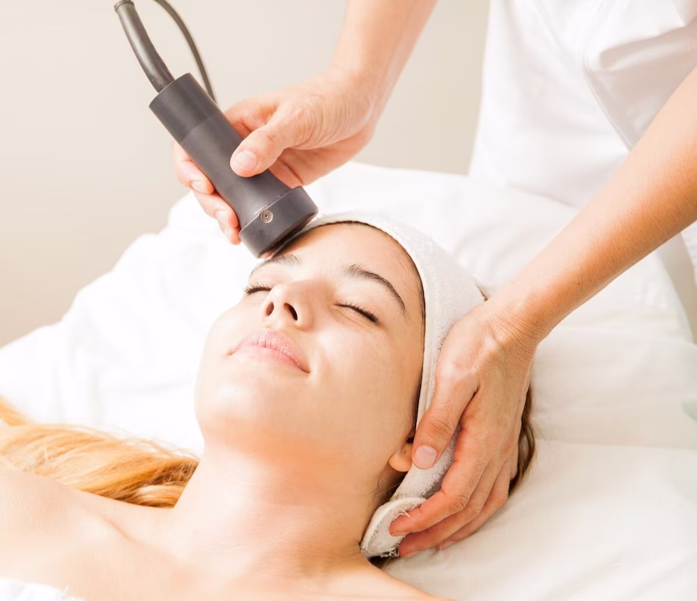 Woman receiving a facial treatment with a handheld device by a professional.