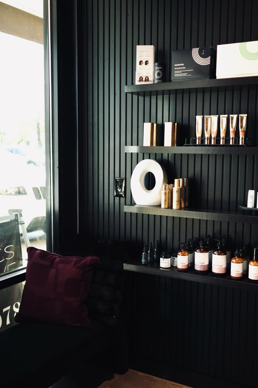 Minimalist spa treatment room with white reclining chair, black storage cabinet under semicircular mirror, and soft lighting.
