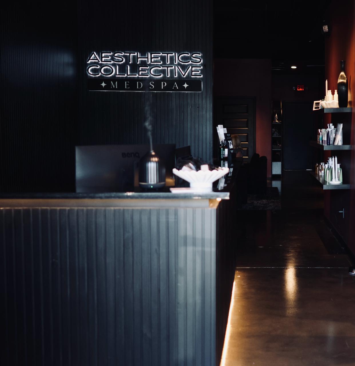 Modern interior with black plush chairs, a large potted plant, marble tile floor, two oval mirrors, and a neon sign that reads 'LET'S GET PIERCED'.