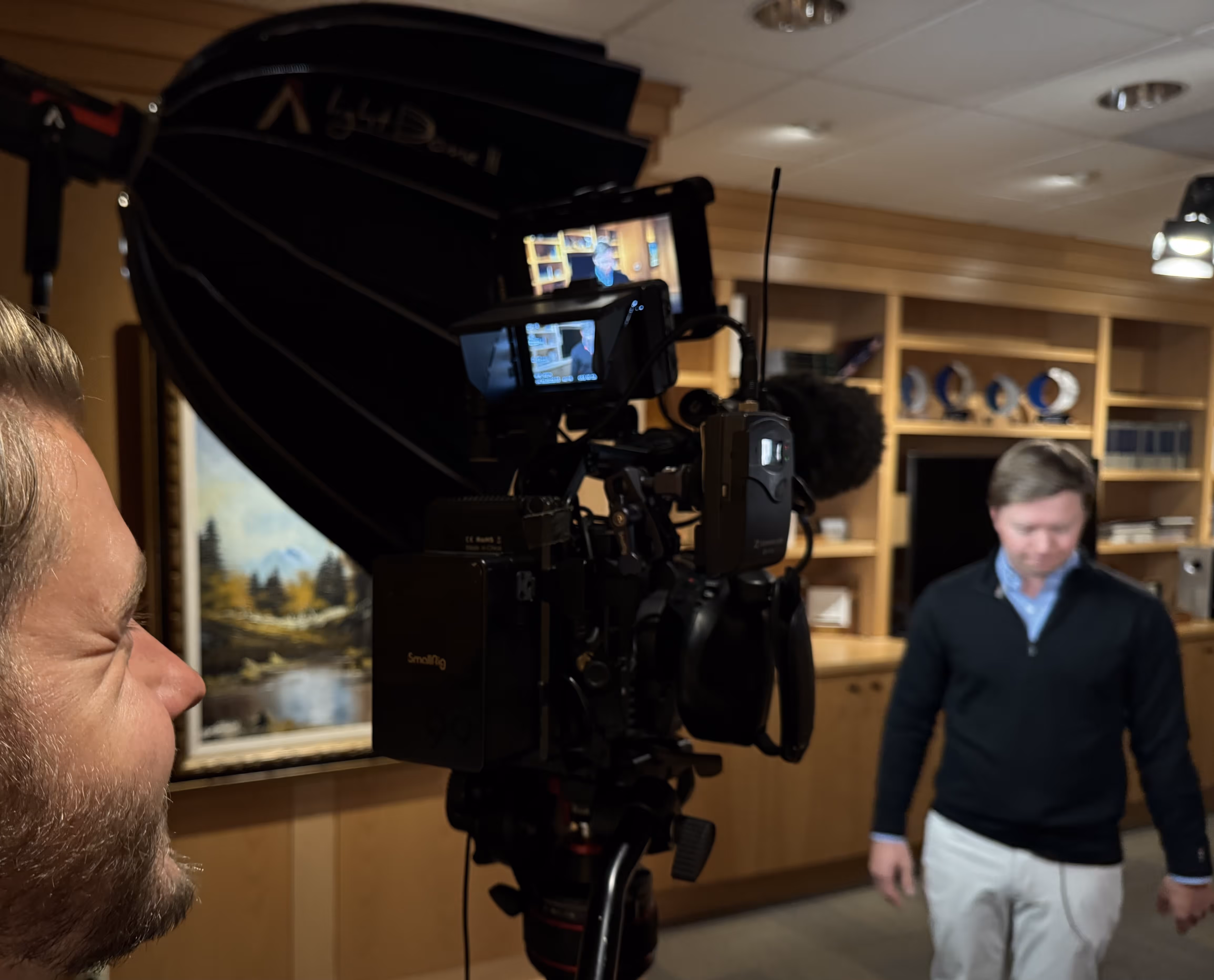 A man from Cutpoint Studio in Eugene, Oregon filming another man walking in a room with wooden shelves, with a large camera setup and lighting equipment.