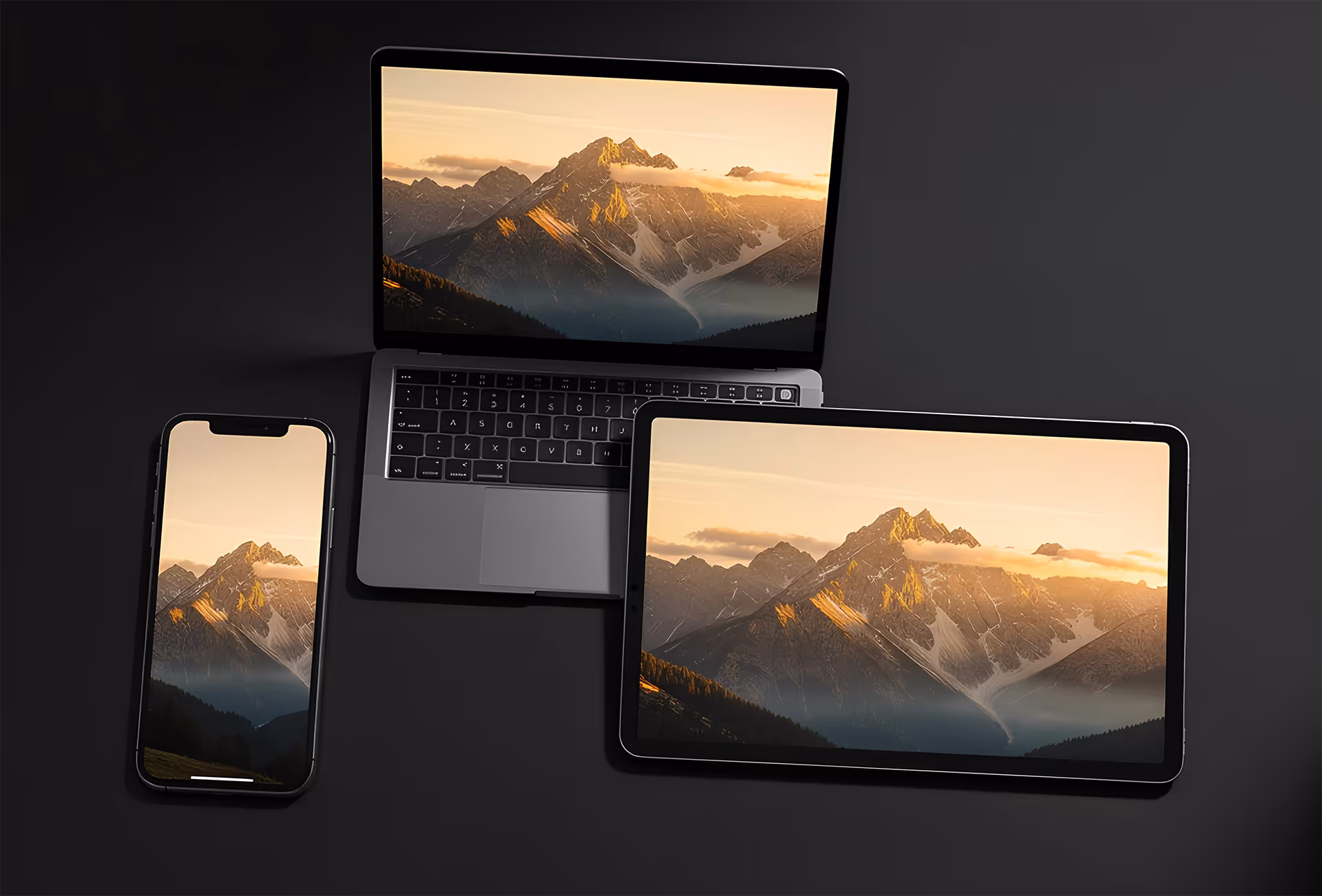 Smartphone, laptop, and tablet displaying the same mountain landscape at sunset on a dark surface.