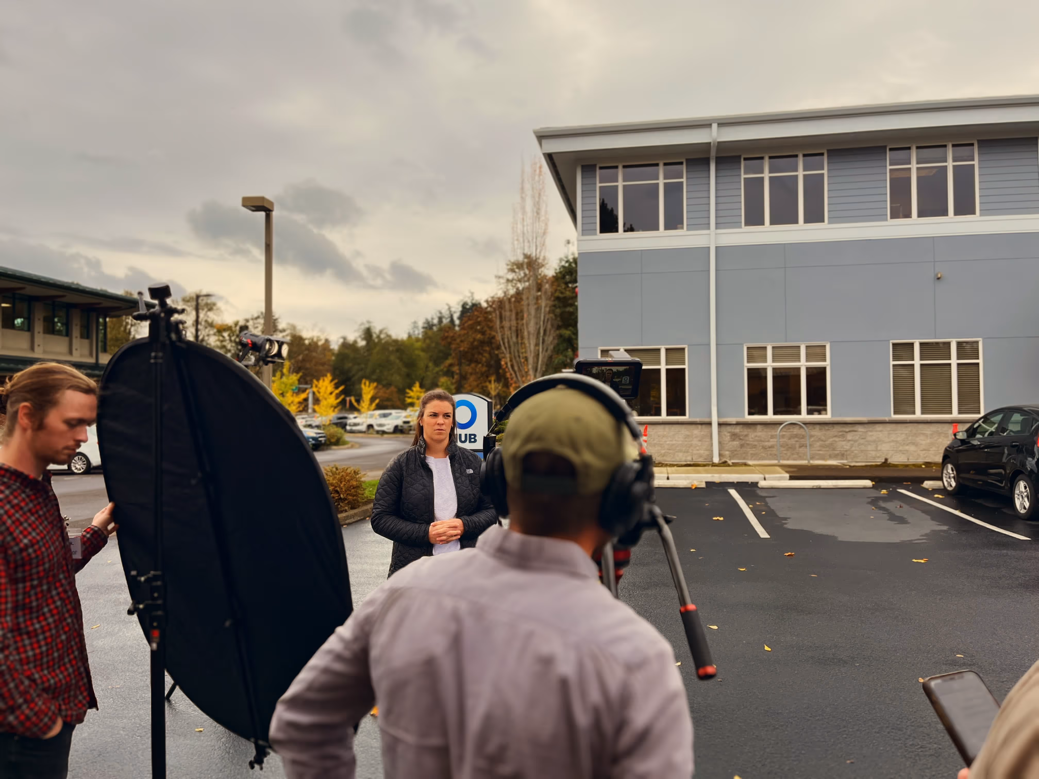 Woman standing outside near a building being recorded by a cameraman from Cutpoint Studio in Eugene, Oregon with a reflector held by another person on a cloudy day.