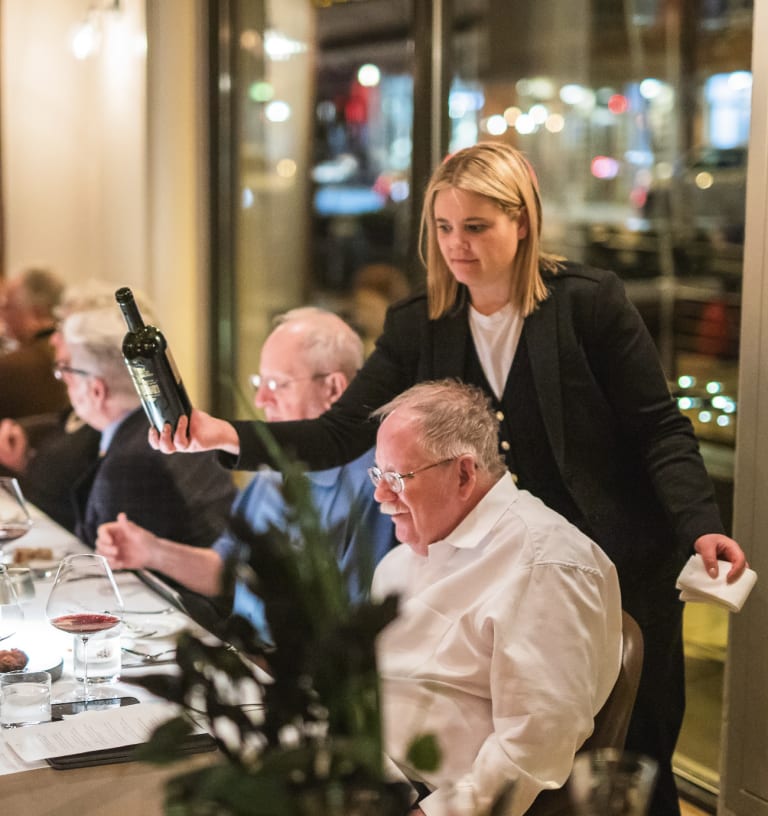 Carlin Karr, Director of Wine and Beverage at Frasca Hospitality Group, presenting a bottle tableside to a guest in the dining room