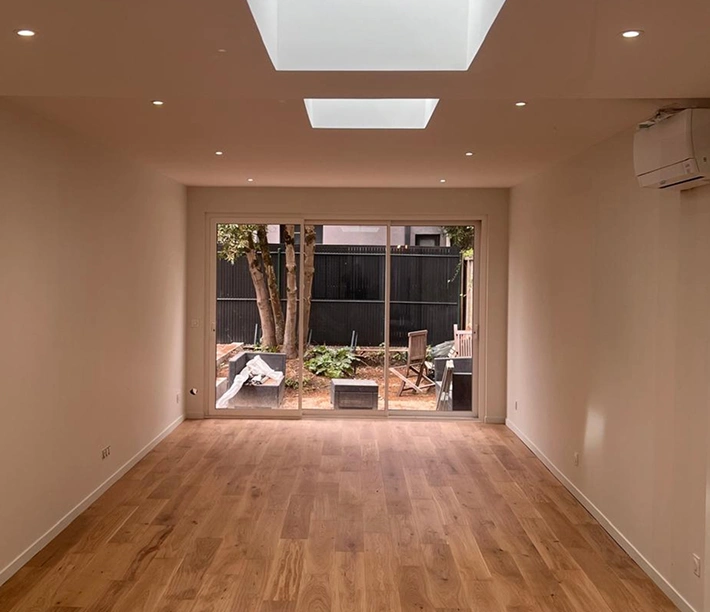 alt="extension maison avec grande pièce de vie, parquet bois, puits de lumière au plafond et baie vitrée à Bordeaux"