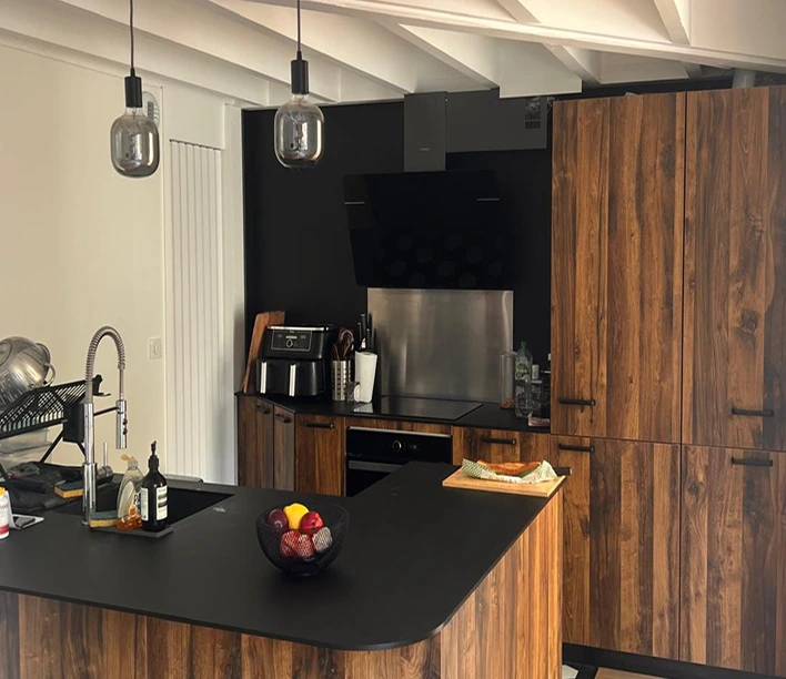 alt="rénovation cuisine avec îlot central noir, meubles en bois et poutres apparentes réalisée à Bordeaux"