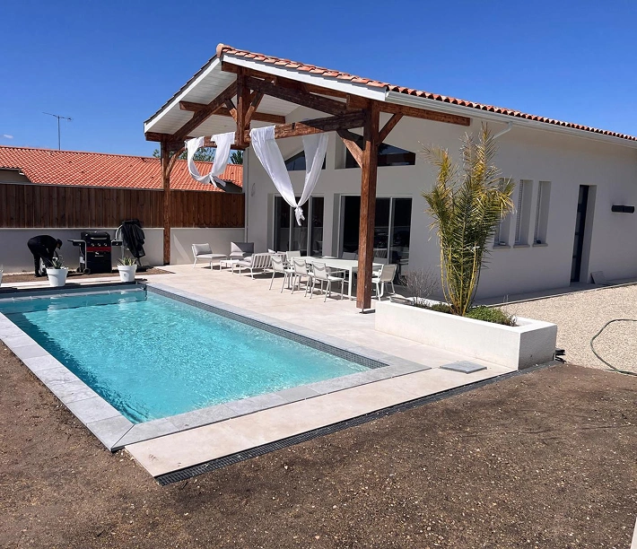 alt="maison rénovée avec terrasse couverte en bois, baies vitrées et piscine extérieure près de Bordeaux"