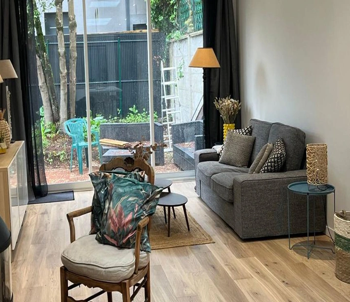 alt="rénovation intérieure d’une pièce de vie avec parquet bois, salon aménagé et baie vitrée donnant sur le jardin à Bordeaux"