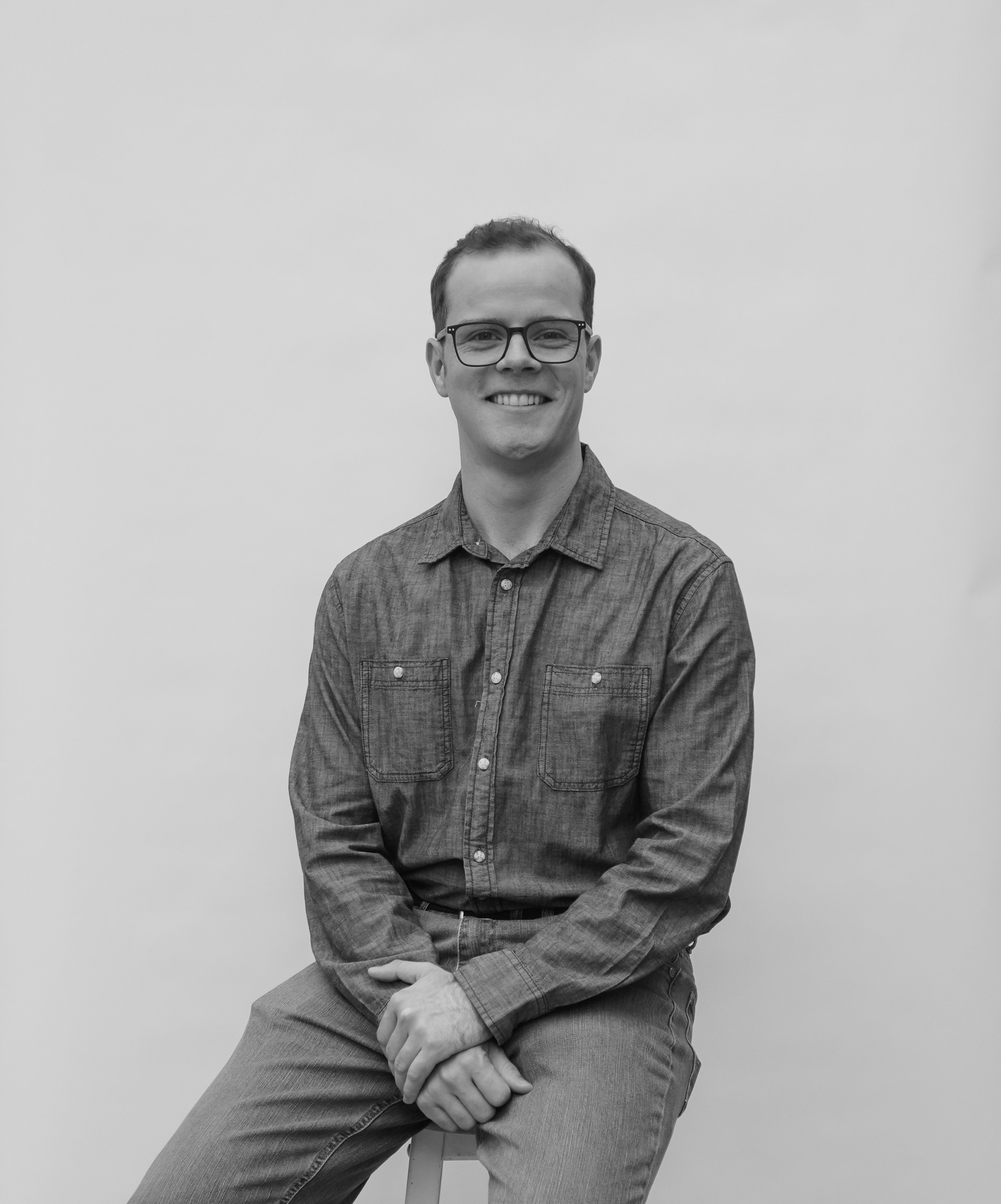 Smiling man, Tyler Crow, wearing glasses and a button-up shirt seated against a plain background.