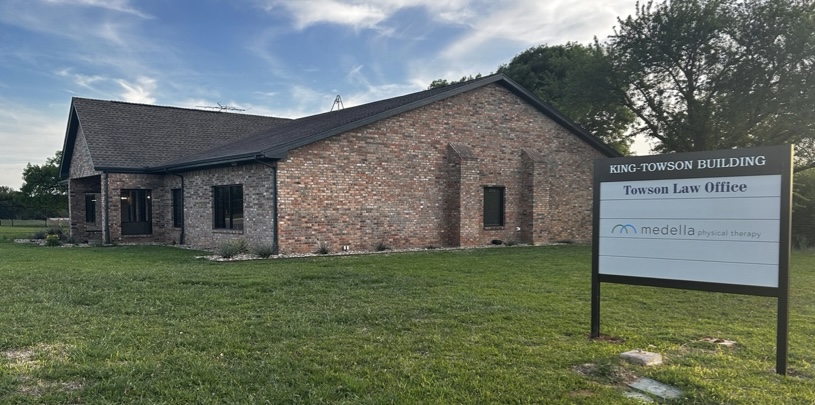 Brick building labeled King-Towson Building with signs for Towson Law Office and Medella Physical Therapy, surrounded by grass and trees under a blue sky.