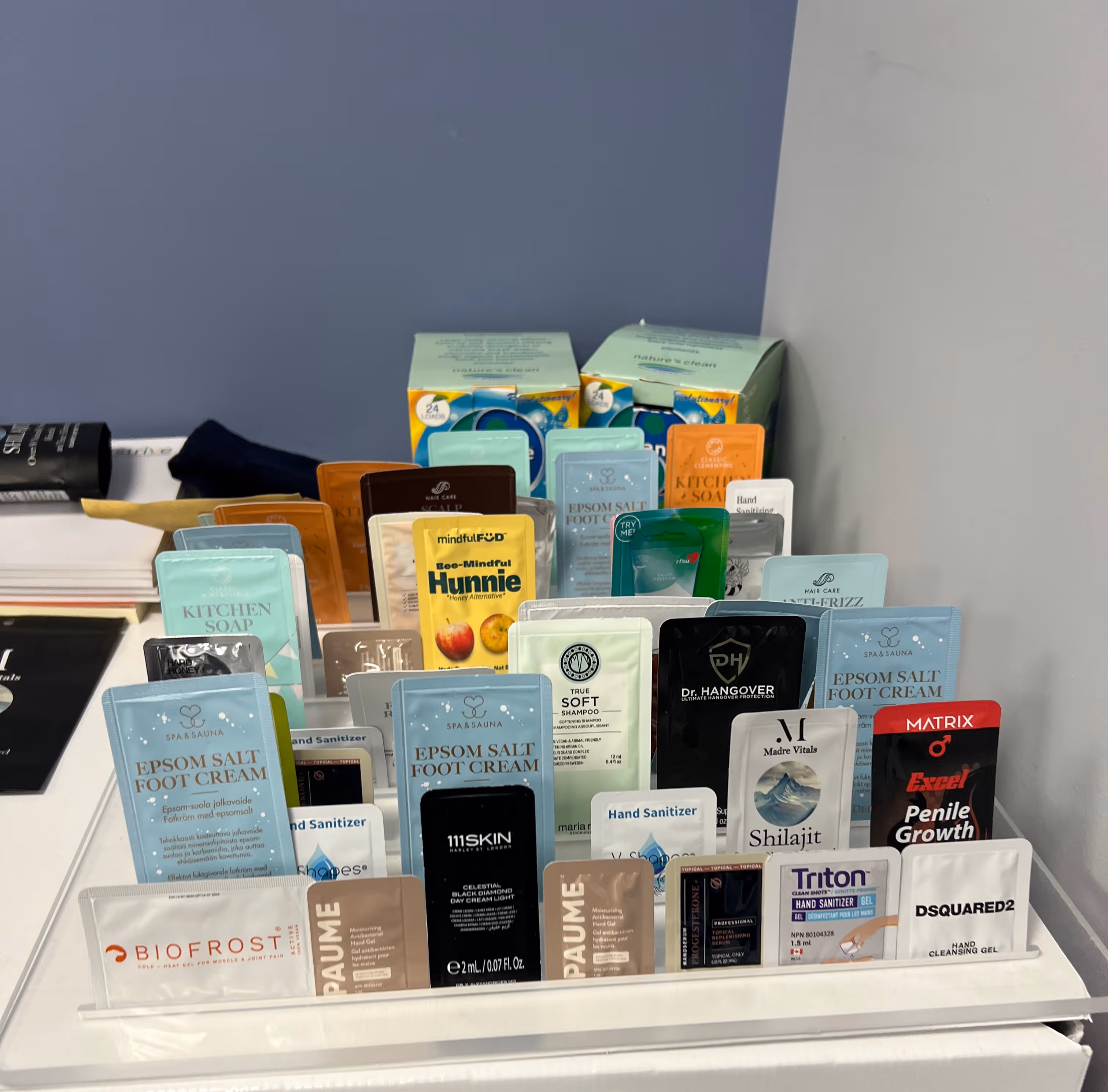 Display of assorted sample sachets including creams, shampoos, sanitizers, and other personal care products.