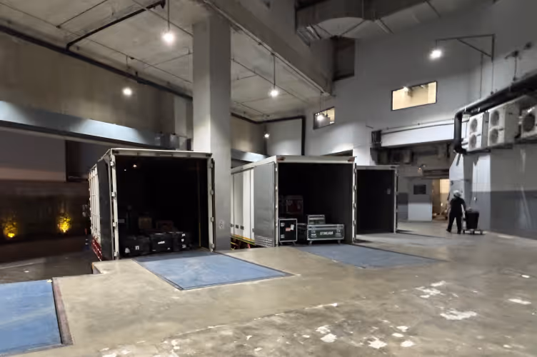 Loading dock area at night with three trailer trucks backed up, their cargo doors open showing equipment inside.
