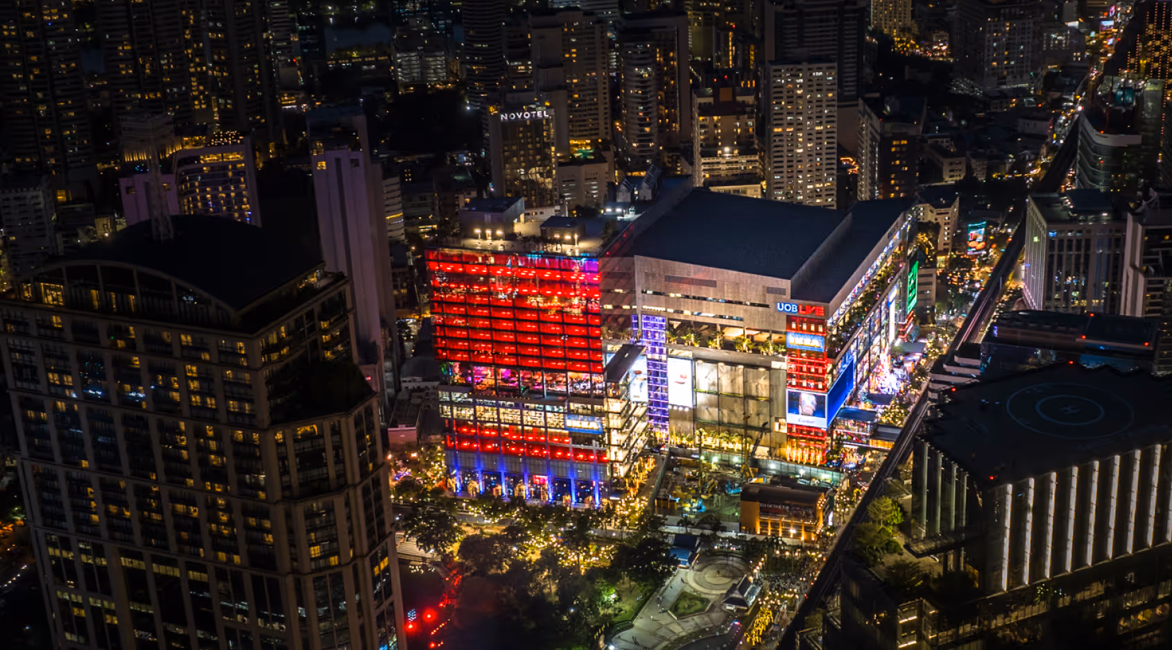 Aerial view of a brightly lit EMSPHERE at night featuring colorful illuminated buildings and busy Sukhumvit Streets