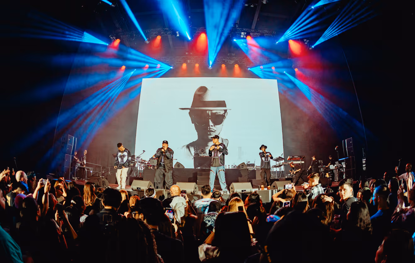 Hip-hop group Thaitanium performing on stage with vibrant blue and red spotlights and a large black-and-white portrait on screen behind them.