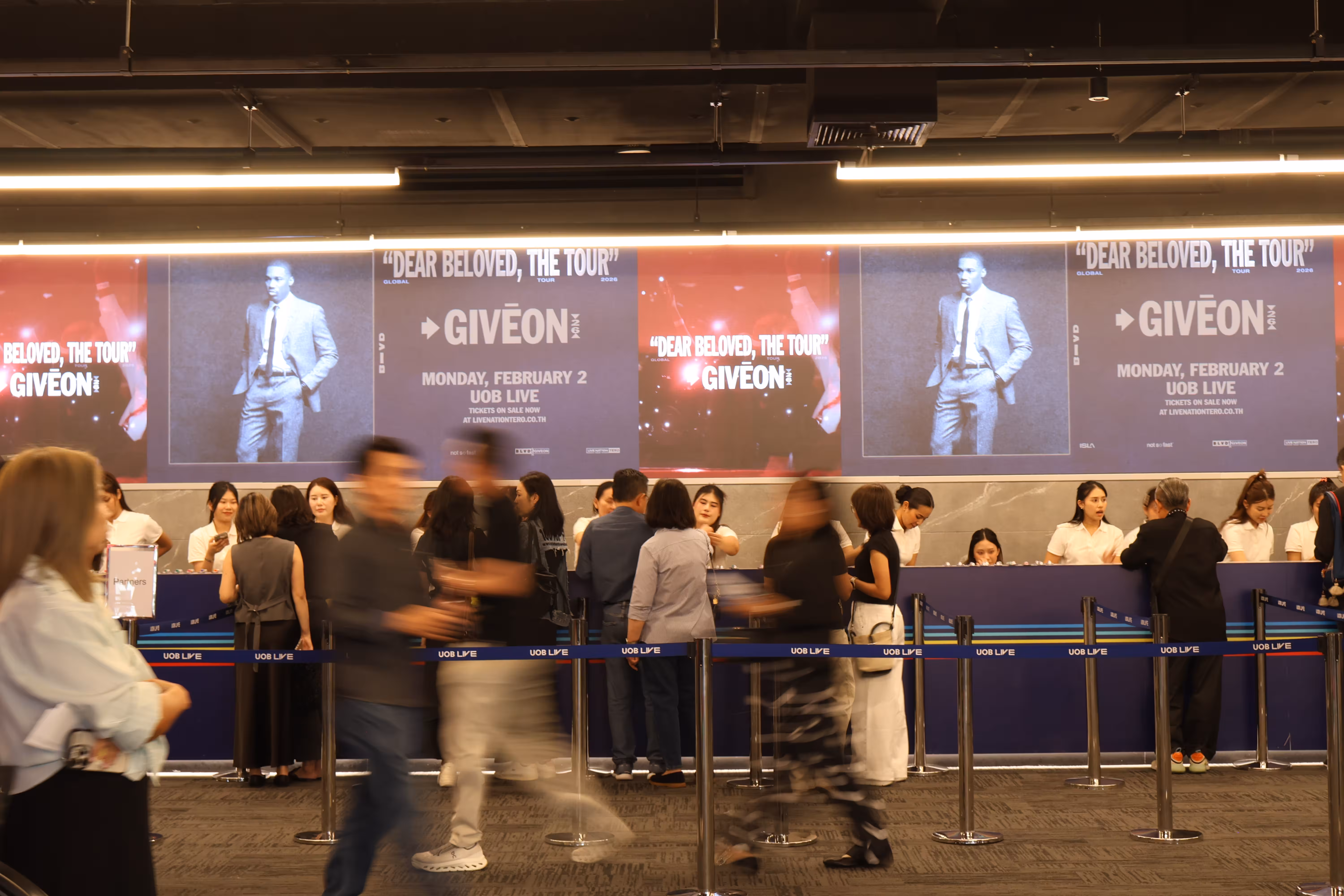 People queue at a ticket counter beneath screens promoting the Giveon 'Dear Beloved, The Tour' event at UOB LIVE