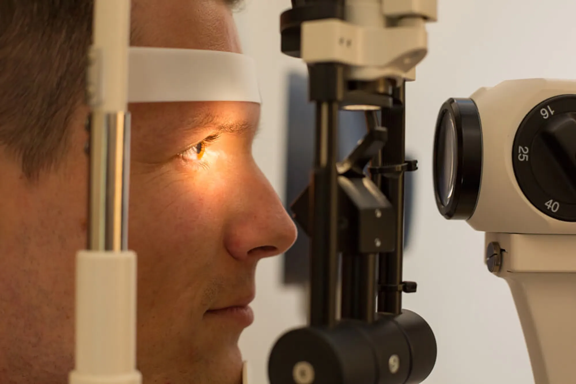 Man undergoing an eye examination using a slit lamp in an optometrist's office.