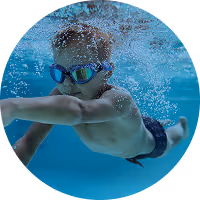 A boy in goggles swimming underwater in a heated indoor pool