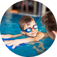 A boy in goggles holding a kickboard at the edge of the pool during a swimming lesson