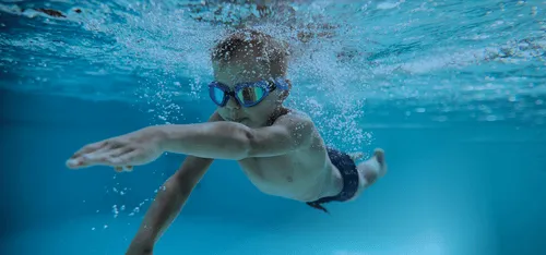 A boy in goggles swimming underwater in a heated indoor pool