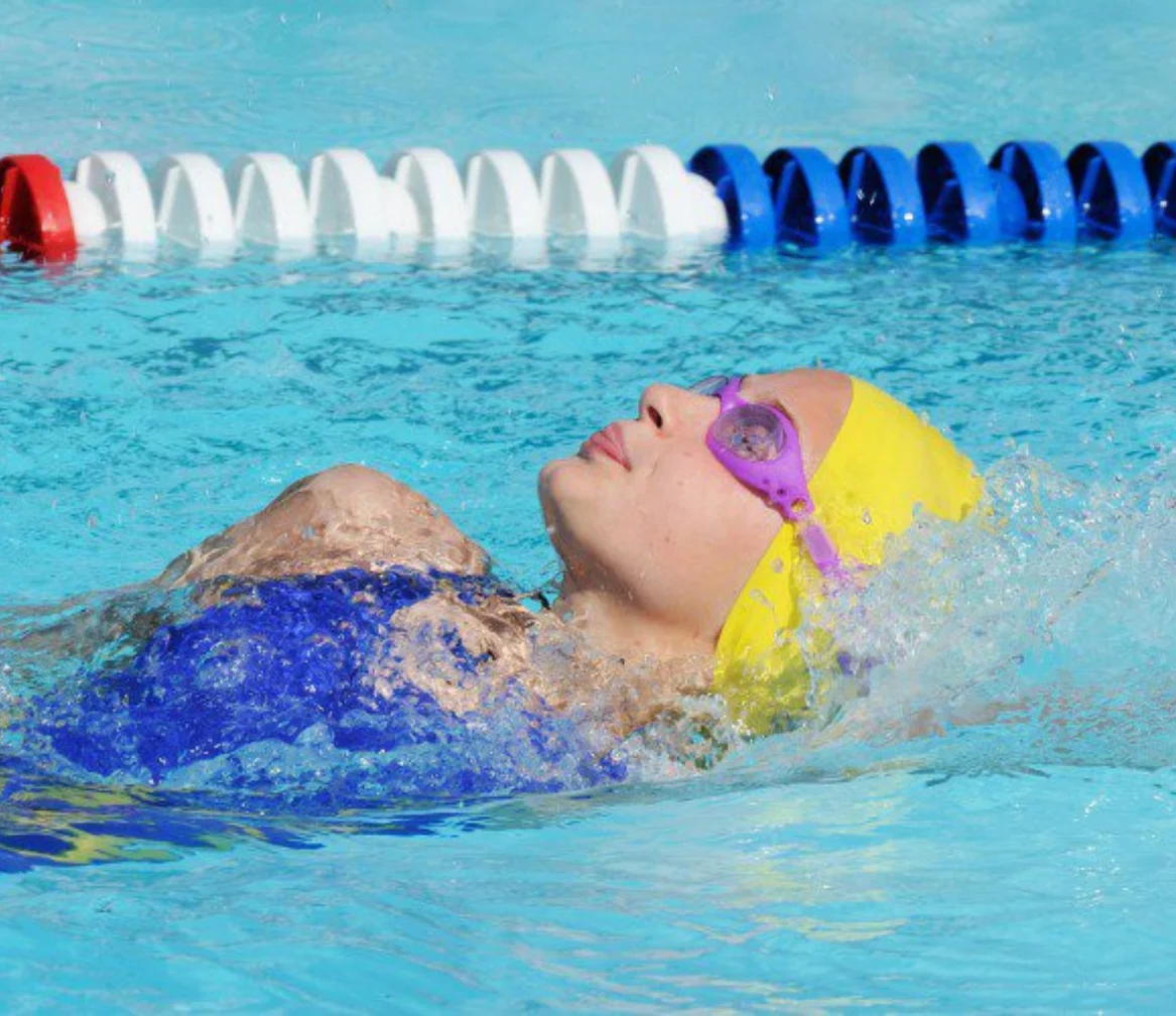 A student in a swimming cap and goggles swimming breaststroke in a marked lane