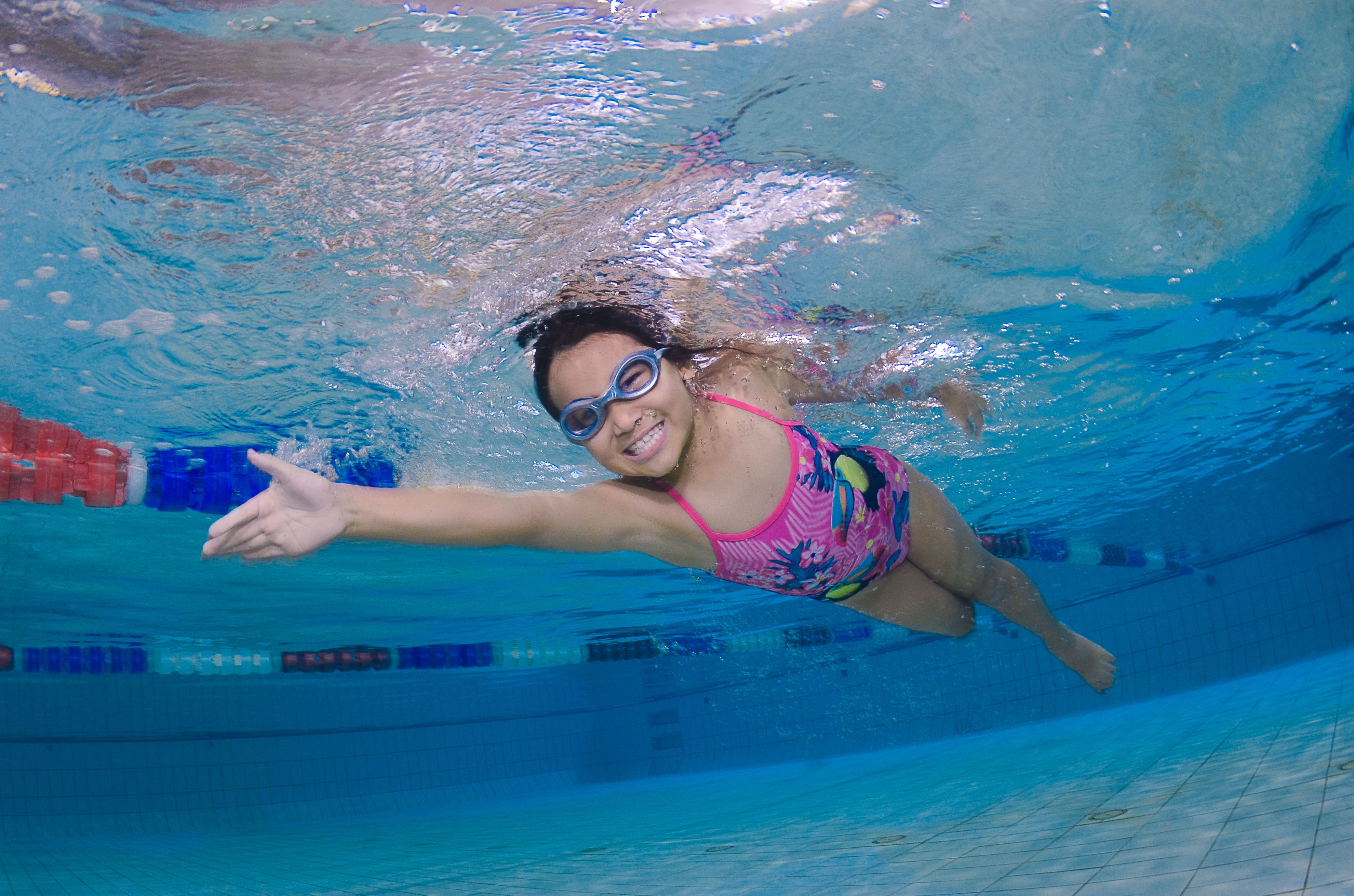 A student in a swimming cap and goggles taking a breath mid stroke