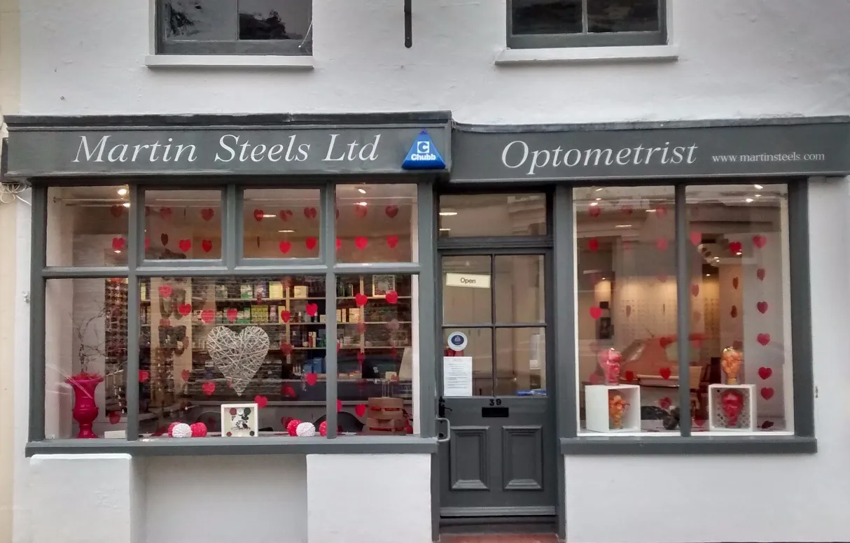 Front view of Martin Steels Ltd Optometrist shop with gray framing and red heart decorations on the windows.
