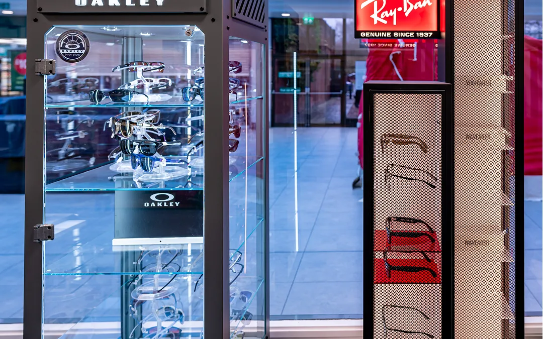 Glass display case with multiple Oakley sunglasses and nearby Ray-Ban signage in a retail store.