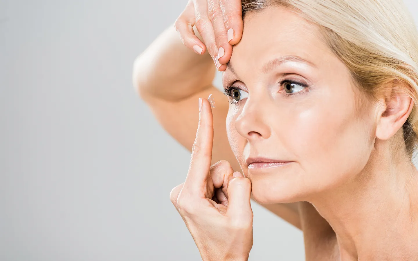 Middle-aged woman holding a contact lens on her finger, preparing to put it in her eye.