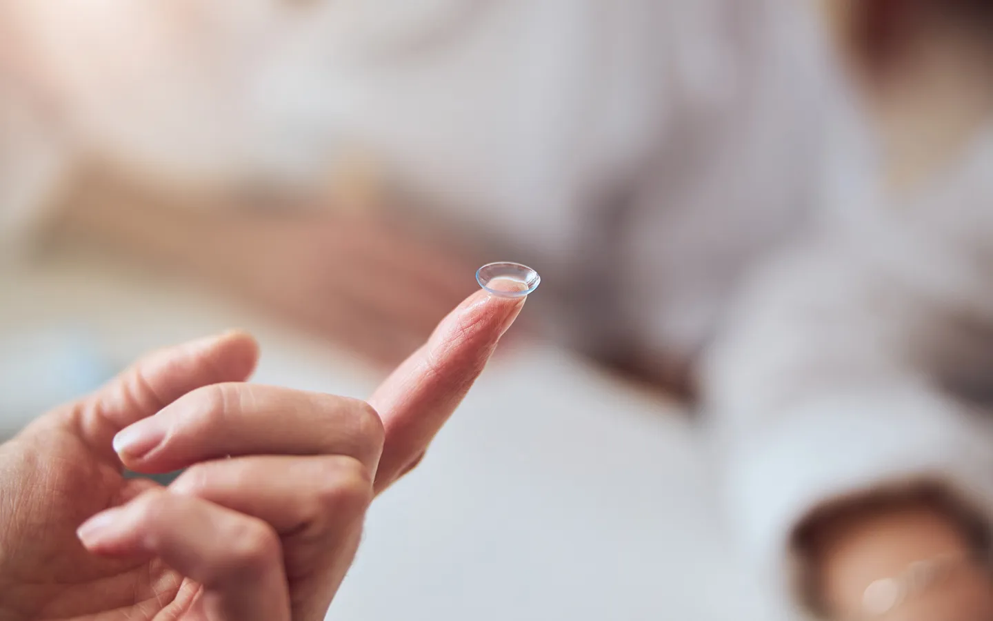 Close-up of a hand holding a transparent contact lens on the fingertip.