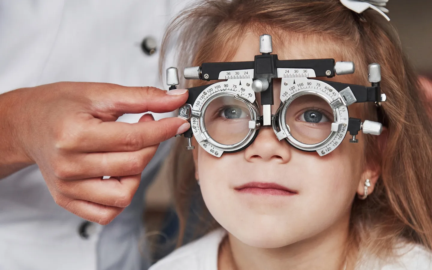 Young girl wearing a trial frame while an eye care professional adjusts it during an eye examination.