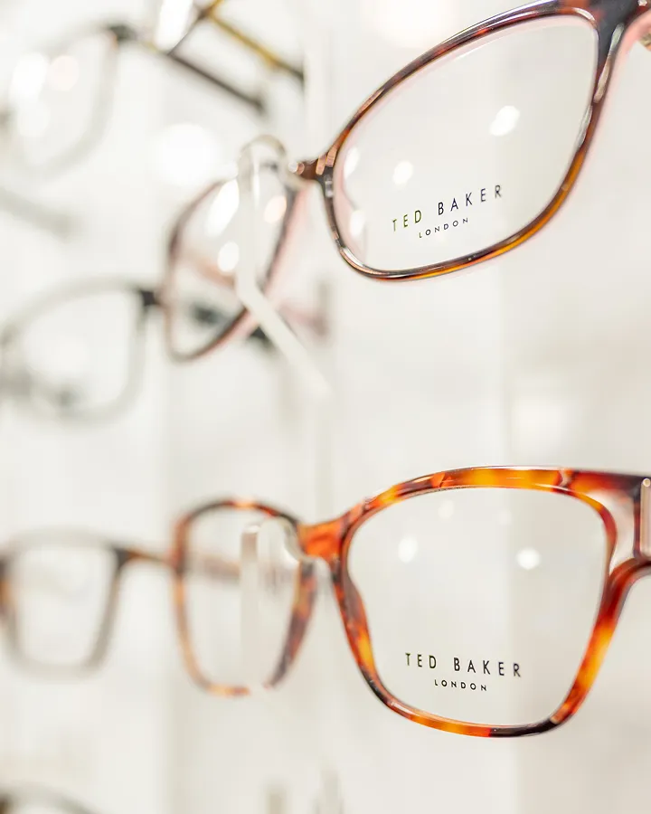 Close-up of Ted Baker London eyeglasses with tortoiseshell frames displayed on a white stand.