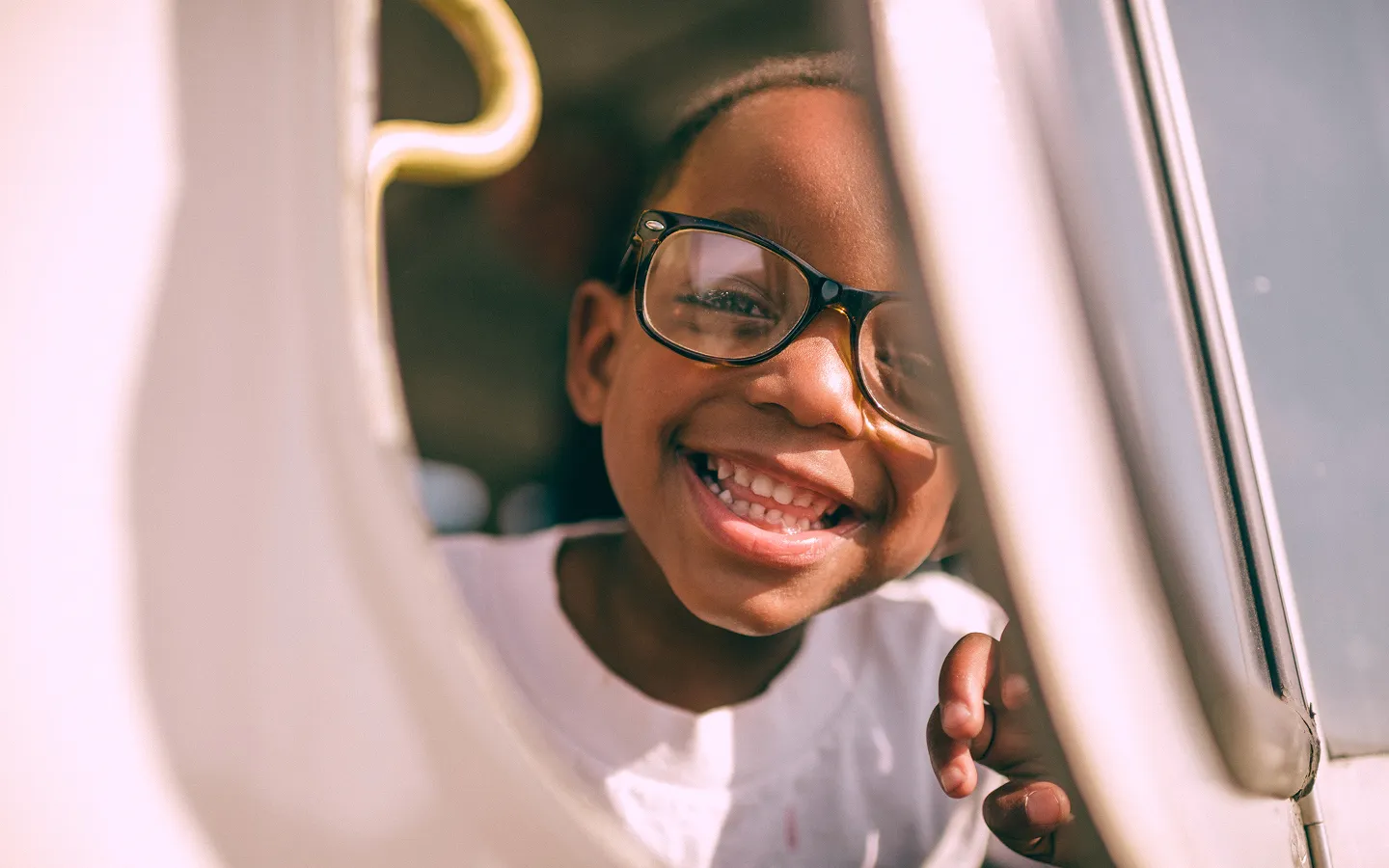 Smiling child wearing large eyeglasses looking through a window.