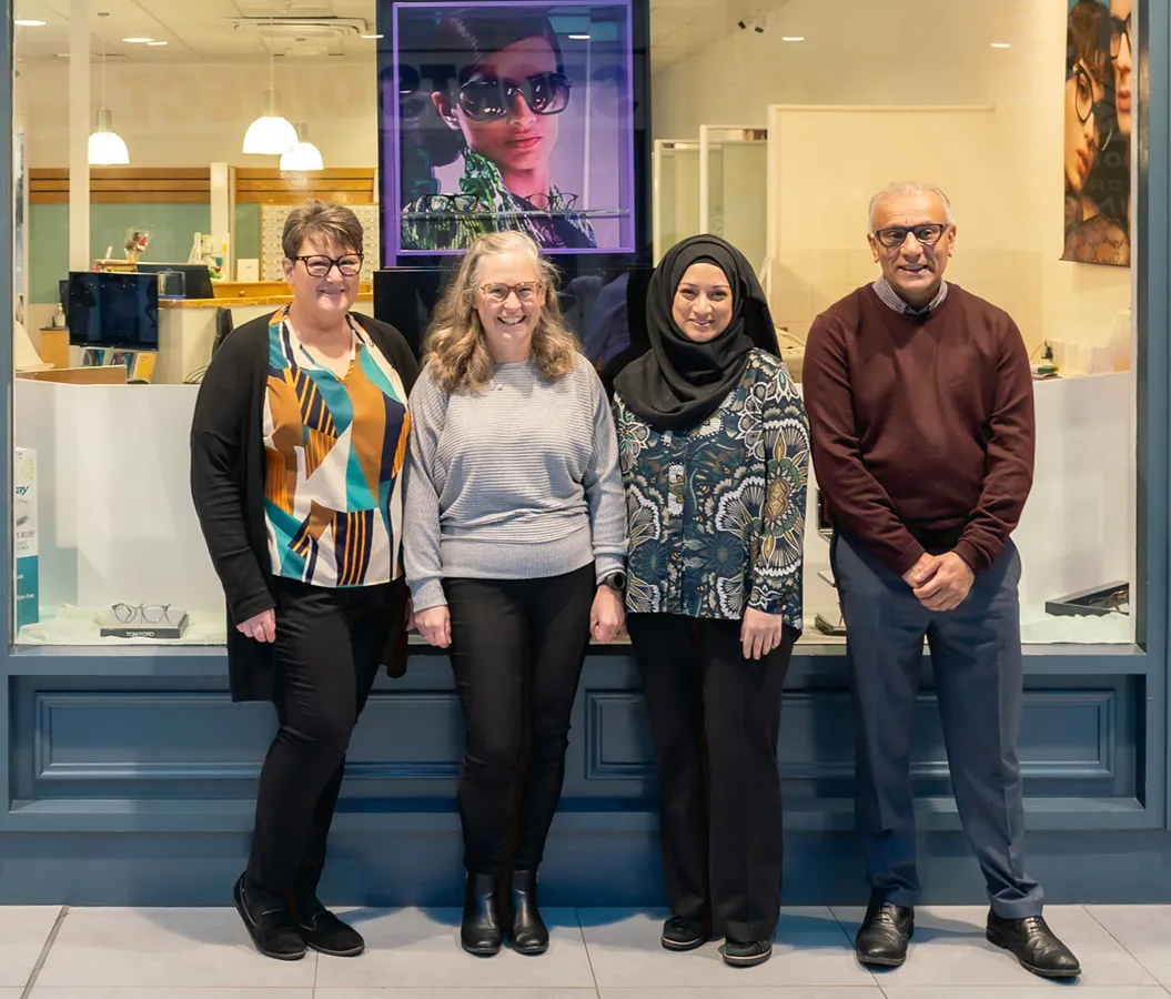 Four diverse adults wearing glasses smiling and standing together in an eyewear store.