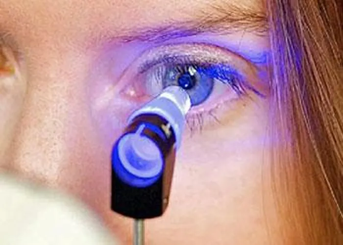 Close-up of a blue eye being examined with a medical device emitting blue light during an eye test.