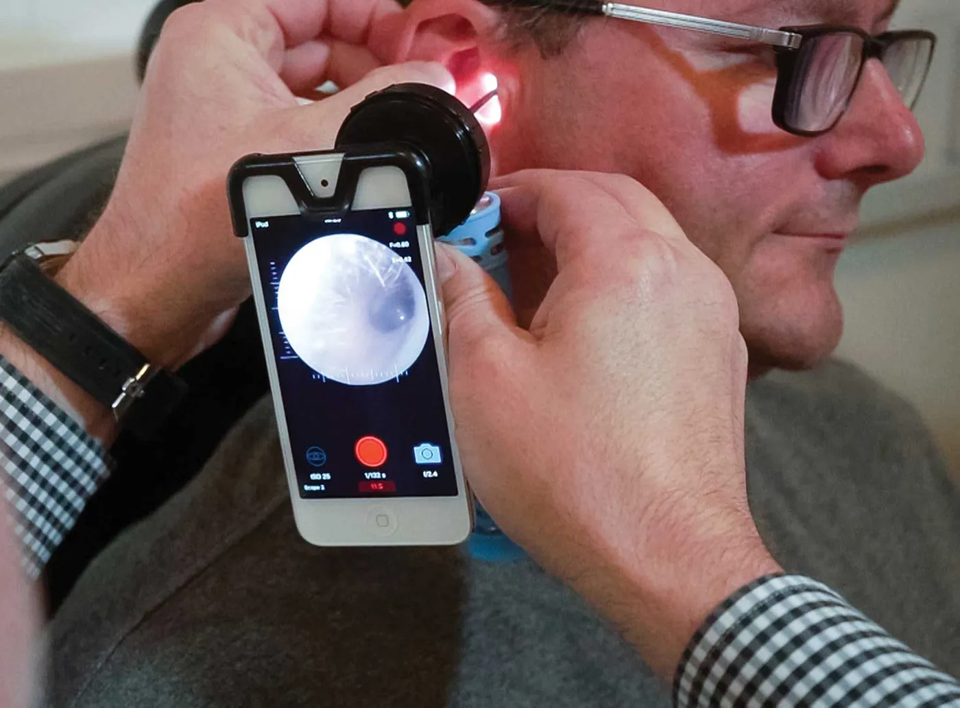 Healthcare professional using a smartphone ear scope to examine a man's ear canal.