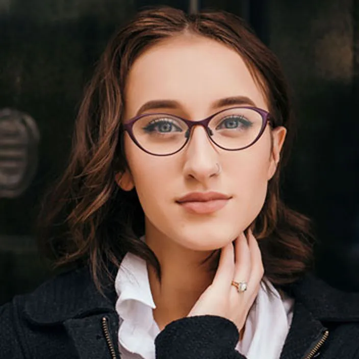 Young woman with brown hair and glasses, wearing a black coat and white shirt.