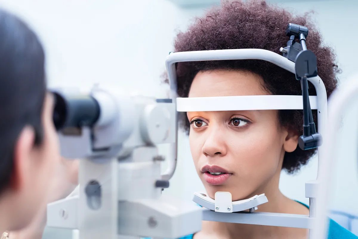 Woman undergoing an eye exam with a slit lamp at an optometrist's office.