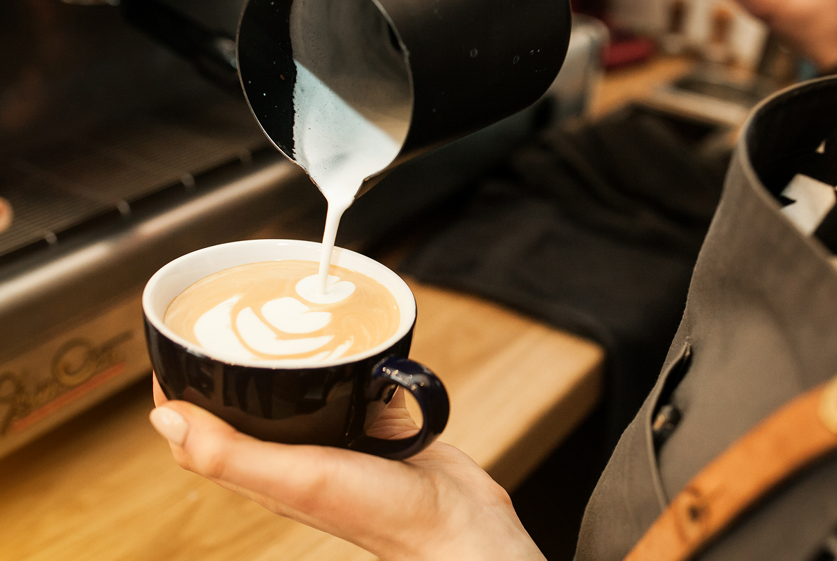 Barista pouring steamed milk into a cup of coffee to create latte art.