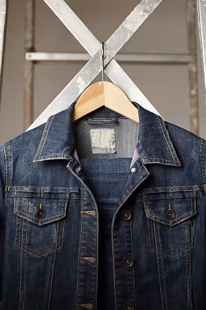 Dark blue denim jacket hanging on a wooden hanger against a metal crossbar background.