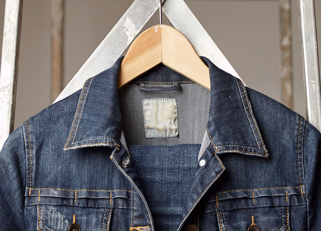 Close-up of a dark blue denim jacket hanging on a wooden hanger.